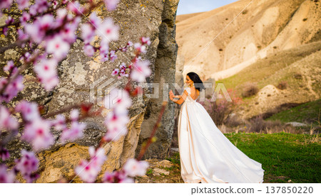 Elegant Bride In Flowing Gown Touching Rock With Pink Spring Blossoms In Foreground 137850220