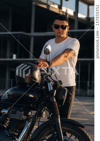 Construction site behind, posing. Man is outdoors with his motorcycle Construction site behind, posing. Man is outdoors with his motorcycle 137850352