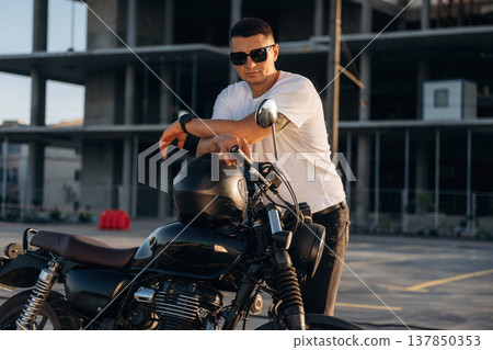 Construction site behind, posing. Man is outdoors with his motorcycle Construction site behind, posing. Man is outdoors with his motorcycle 137850353