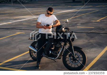 Smartphone is in hands. Man is outdoors with his motorcycle 137850359