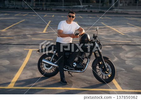 Smartphone is in hands. Man is outdoors with his motorcycle Smartphone is in hands. Man is outdoors with his motorcycle 137850362