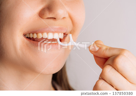 Woman using floss pick between teeth, close up oral care routine 137850380