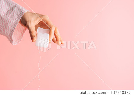 Hand pulling dental floss from a white container on pink background, oral care routine with copy space Hand pulling dental floss from a white container on pink background, oral care routine with copy space 137850382