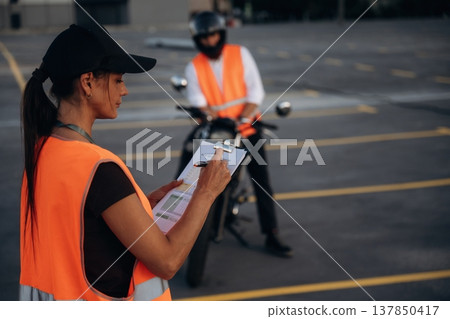 Writing the results into notepad. Motorcycle driving license exam. Man and woman are in uniforms Writing the results into notepad. Motorcycle driving license exam. Man and woman are in uniforms 137850417