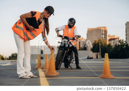 Placing the cones. Motorcycle driving license exam. Man and woman are in uniforms Placing the cones. Motorcycle driving license exam. Man and woman are in uniforms 137850422