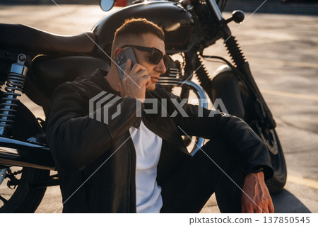 Having conversation by the phone. Man is outdoors with his motorcycle Having conversation by the phone. Man is outdoors with his motorcycle 137850545