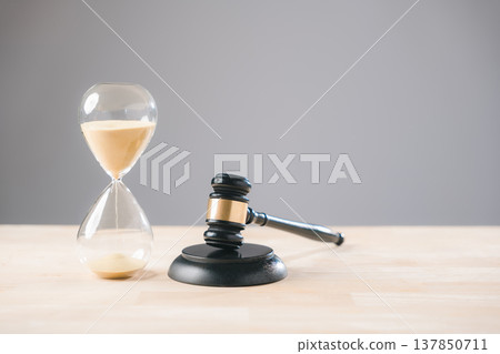 Hourglass displays passing time and legal gavel signifies law and justice, representing crucial deadlines for judge or lawyer in court cases demanding prompt resolution Hourglass displays passing time and legal gavel signifies law and justice, representing crucial deadlines for judge or lawyer in court cases demanding prompt resolution 137850711