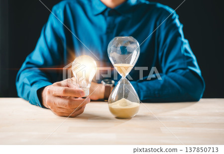 Man holding bright lightbulb idea and hourglass with flowing sand, showing time management for business concept, innovation, urgent deadline, emphasizing timer countdown Man holding bright lightbulb idea and hourglass with flowing sand, showing time management for business concept, innovation, urgent deadline, emphasizing timer countdown 137850713