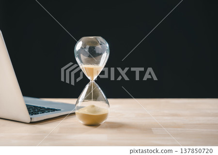 Hourglass, time glass, hour, sand clock, timer visualize business growth concept, urgency for deadline countdown, laptop rests on wooden desk to optimize business progress 137850720