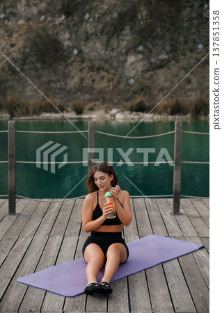 Pretty Woman Drinking Water After Yoga Workout Outdoors At Lake. Hydration And Recovery Concept Pretty Woman Drinking Water After Yoga Workout Outdoors At Lake. Hydration And Recovery Concept 137851358