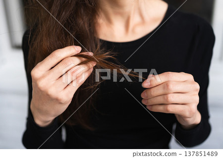 womans hands examine the ends of her long brown hair in close-up. personal care beauty routine health hair damage check concept womans hands examine the ends of her long brown hair in close-up. personal care beauty routine health hair damage check concept 137851489