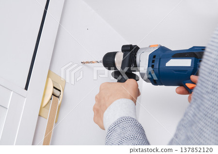 a man drills a hole in a wall with a drill a man drills a hole in a wall with a drill 137852120