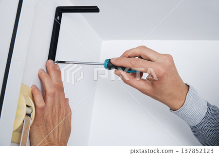 a man tightens a screw on a wall bracket 137852123