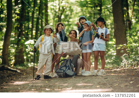Path searching, sitting and reading a map. Woman is doing tour for group of kids in the forest Path searching, sitting and reading a map. Woman is doing tour for group of kids in the forest 137852201