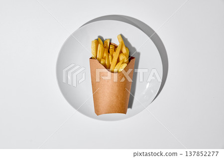 French fries in paper box placed on white plate on clean white background top view with strong shadows French fries in paper box placed on white plate on clean white background top view with strong shadows 137852277