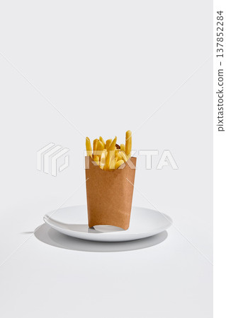 French fries served in paper box placed on white plate on clean white background with strong shadows 137852284