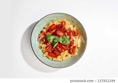 Fusilli pasta with tomato sauce, cherry tomatoes and basil served on ceramic plate on white background. Fusilli pasta with tomato sauce, cherry tomatoes and basil served on ceramic plate on white background. 137852294