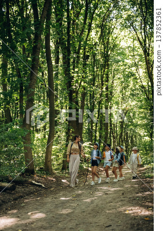 Straight path. Woman is doing tour for group of kids in the forest Straight path. Woman is doing tour for group of kids in the forest 137852361