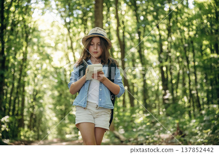 Small notepad is in hands. Young girl hiker is in the forest Small notepad is in hands. Young girl hiker is in the forest 137852442