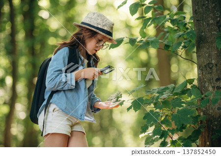 Scientific project research, with magnifying glass and plants. Young girl hiker is in the forest Scientific project research, with magnifying glass and plants. Young girl hiker is in the forest 137852450