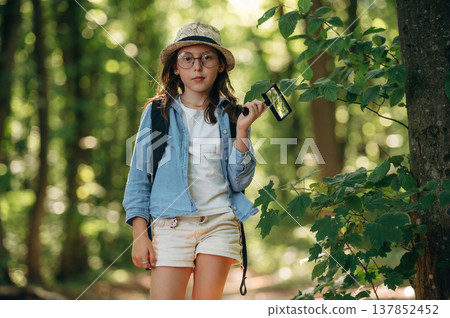 Biological project, with magnifying glass. Young girl hiker is in the forest Biological project, with magnifying glass. Young girl hiker is in the forest 137852452