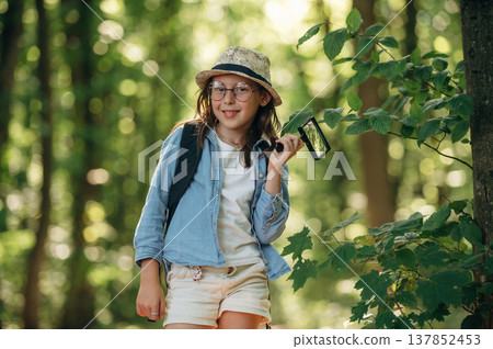 Biological project, with magnifying glass. Young girl hiker is in the forest 137852453