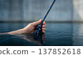 Close-up of a hand gripping a thick blue climbing rope emerging from dark water 137852618