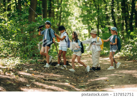 Trusting the girl with a map. Group of children in the forest on a hike Trusting the girl with a map. Group of children in the forest on a hike 137852751