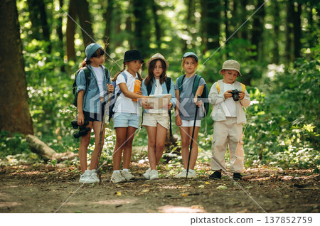 Camera and paper map in hands. Group of children in the forest on a hike 137852759