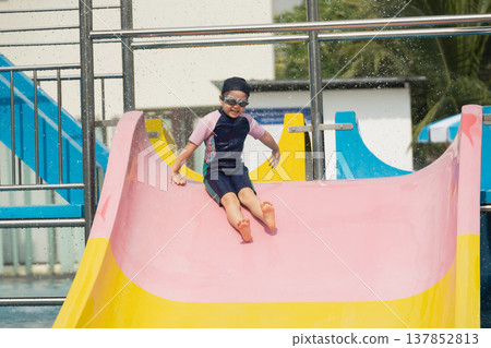 Young child enjoying colorful waterslide at summer water park, cheerful expression and water splashes, perfect for family-friendly themes and leisure activities Young child enjoying colorful waterslide at summer water park, cheerful expression and water splashes, perfect for family-friendly themes and leisure activities 137852813