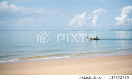 Serene Beach Scene with Gentle Waves and a Traditional Fishing Boat Under Clear Blue Skies and Fluffy White Clouds on a Calm Day Serene Beach Scene with Gentle Waves and a Traditional Fishing Boat Under Clear Blue Skies and Fluffy White Clouds on a Calm Day 137852819