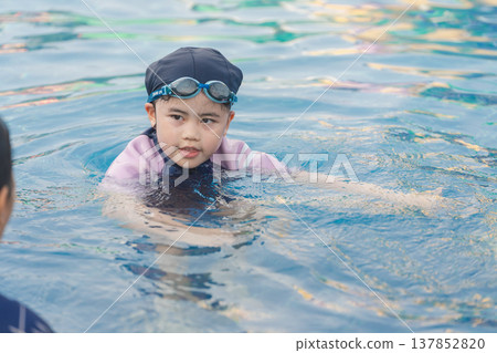 Young child in a swimming pool wearing a swim cap and goggles, practicing swimming strokes and enjoying aquatic fun in sunny weather 137852820