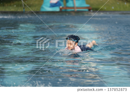 Happy Child Swimming in Clear Water of Swimming Pool During Summer Day Fun with Goggles and Swimwear 137852873