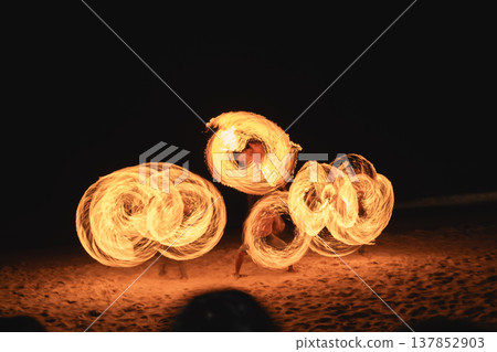 Captivating Fire Dance Performance at Night on the Beach with Glowing Flames and Vibrant Swirls Creating a Magical Atmosphere for Spectators Captivating Fire Dance Performance at Night on the Beach with Glowing Flames and Vibrant Swirls Creating a Magical Atmosphere for Spectators 137852903