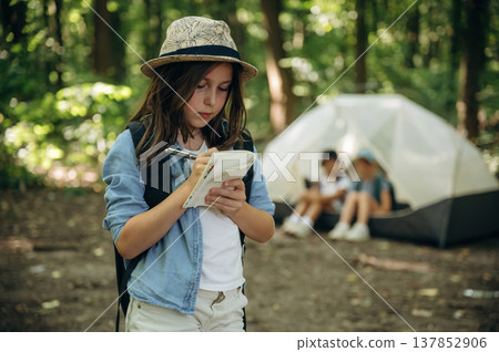 Focused, writing information into notepad. Girls kids are in the forest, hike conception Focused, writing information into notepad. Girls kids are in the forest, hike conception 137852906