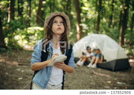 Pen and notepad is in hands. Girls kids are in the forest, hike conception 137852908