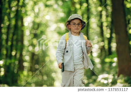Front view, walking. Cute little boy hiker is in the forest Front view, walking. Cute little boy hiker is in the forest 137853117