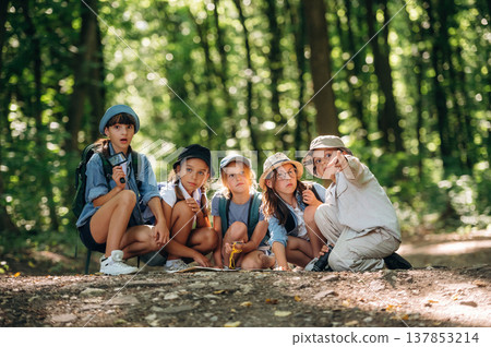 Showing the way, sitting on the ground. Group of children in the forest on a hike Showing the way, sitting on the ground. Group of children in the forest on a hike 137853214