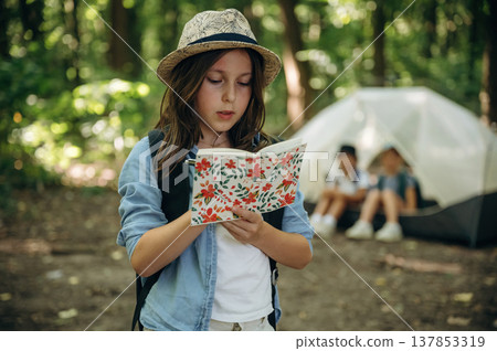 Notepad and pen is in hands. Girls kids are in the forest, hike conception 137853319