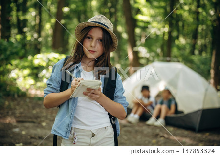 Notepad and pen is in hands. Girls kids are in the forest, hike conception Notepad and pen is in hands. Girls kids are in the forest, hike conception 137853324
