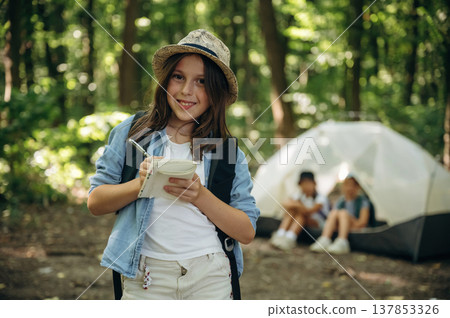 Notepad and pen is in hands. Girls kids are in the forest, hike conception Notepad and pen is in hands. Girls kids are in the forest, hike conception 137853326