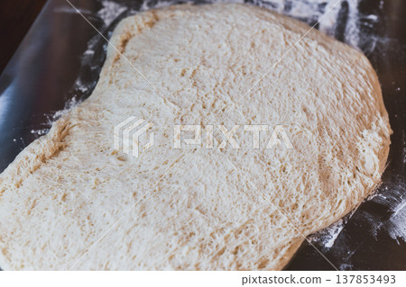 Freshly proofed bread dough with airy texture spread on a floured surface, ready for baking. 137853493