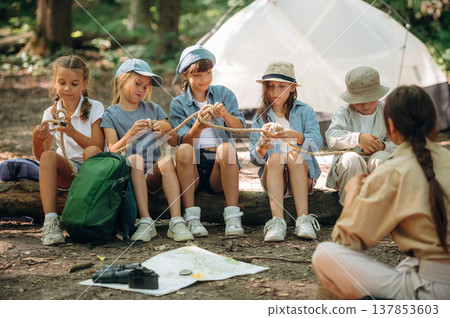 Survival tips, sitting at camp. Woman is doing tour for group of kids in the forest Survival tips, sitting at camp. Woman is doing tour for group of kids in the forest 137853603