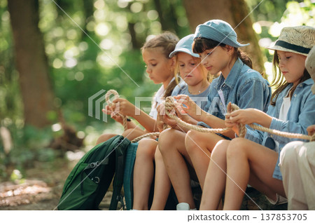 Holding the rope, sitting. Group of children in the forest on a hike Holding the rope, sitting. Group of children in the forest on a hike 137853705