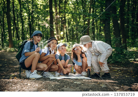 Old fashioned paper map on the ground. Group of children in the forest on a hike Old fashioned paper map on the ground. Group of children in the forest on a hike 137853719