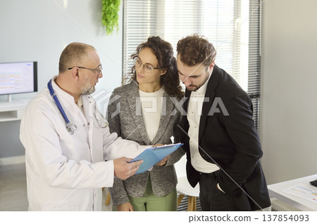 Doctor reviewing medical results with couple in clinic, discussing patient options 137854093
