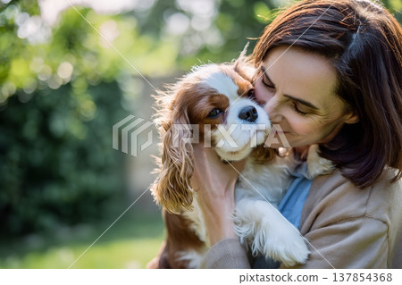 A woman hugs a Cavalier King Charles Spaniel dog outdoors in the sunlight 137854368