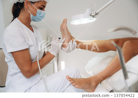 View from the side, doing peeling. Podiatrist with client in clinic View from the side, doing peeling. Podiatrist with client in clinic 137854422