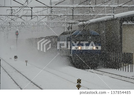 A long northbound freight train pulled by an EF65 locomotive passes through Hikone Station on the Tokaido Main Line in the snow. 137854485