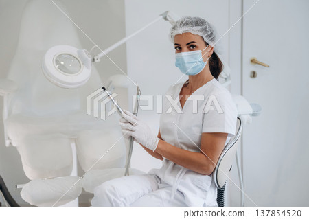 In protective mask. Podiatrist is in the clinic with equipment In protective mask. Podiatrist is in the clinic with equipment 137854520